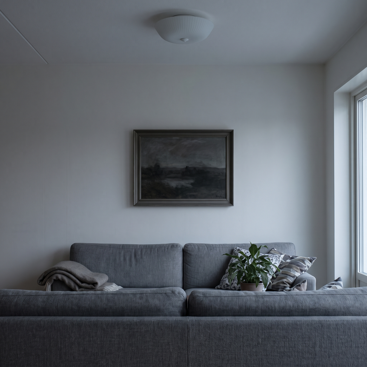 Bildet over sofaen i flatt taklys en novemberettermiddag – fargene er grå
